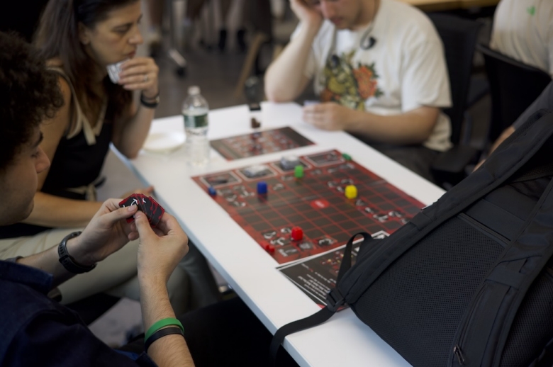 Group of Tisch Summer High school Game Design students sit at a table playing a board game during a game design class.